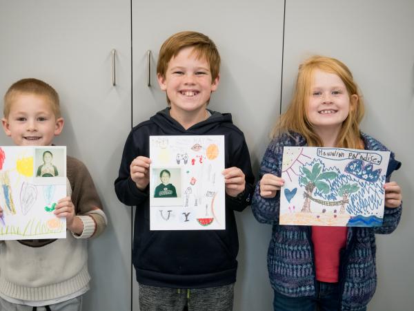 Three Children holding their Polaroid Portraits on matteboard frames they decorated. 